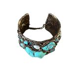 Wide handmade turquoise cuff bracelet featuring large blue-green stones, pearl accents, intricate antique bronze-tone sculptural detailing and safety chain.