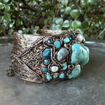 Wide handmade turquoise cuff bracelet featuring large blue-green stones, pearl accents, intricate antique bronze-tone sculptural detailing and safety chain.