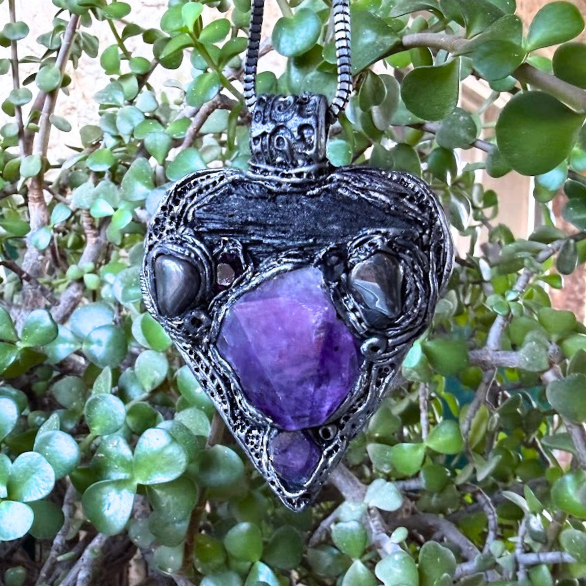 Sculptural heart pendant necklace with central purple Amethyst, dark textured setting and polished Hematite stones.