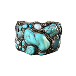 Wide handmade turquoise cuff bracelet featuring large blue-green stones, pearl accents, intricate antique bronze-tone sculptural detailing and safety chain.
