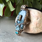 Handmade Blue Apatite pendant necklace combining raw and polished blue gemstones with contrasting textures in an ornate antique bronze-tone polymer clay setting on a black cord.