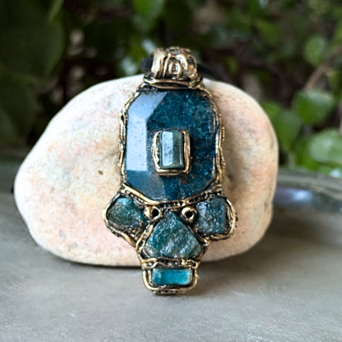Handmade Blue Apatite pendant necklace combining raw and polished blue gemstones with contrasting textures in an ornate antique bronze-tone polymer clay setting on a black cord.