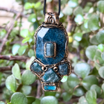 Handmade Blue Apatite pendant necklace combining raw and polished blue gemstones with contrasting textures in an ornate antique bronze-tone polymer clay setting on a black cord.