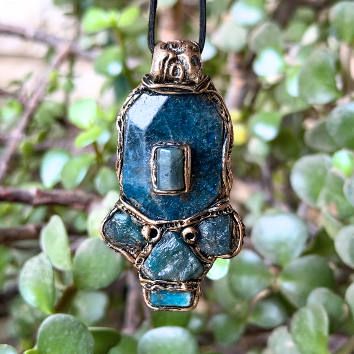 Handmade Blue Apatite pendant necklace combining raw and polished blue gemstones with contrasting textures in an ornate antique bronze-tone polymer clay setting on a black cord.