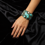 Wide handmade turquoise cuff bracelet featuring large blue-green stones, pearl accents, intricate antique bronze-tone sculptural detailing and safety chain.